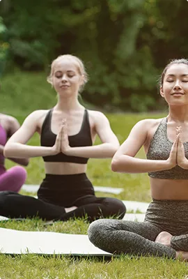 Two women meditating cross-legged outdoors on yoga mats