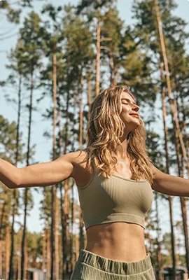 Woman stretching with arms open among tall pine trees